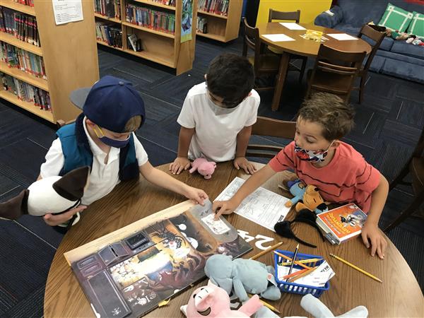 Three boys look at a book on a table